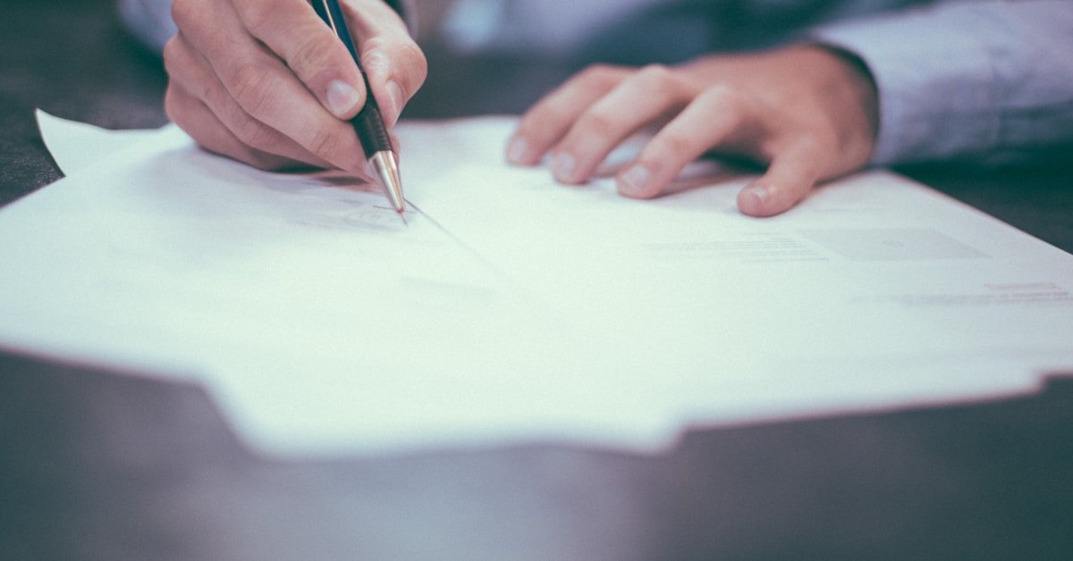 Person filling out a paper form by hand, pen in hand